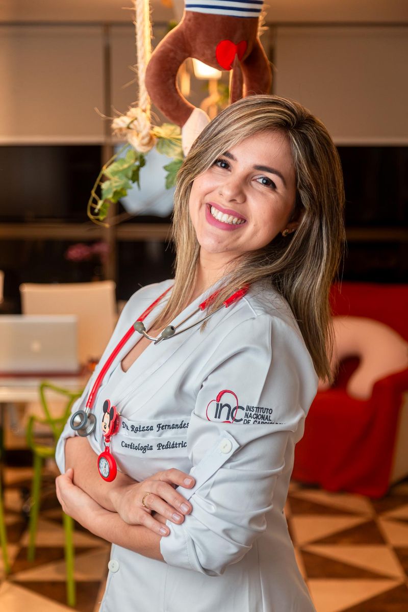 Dra. Raizza Fernandes sorrindo, de jaleco e estetoscópio, no consultório
